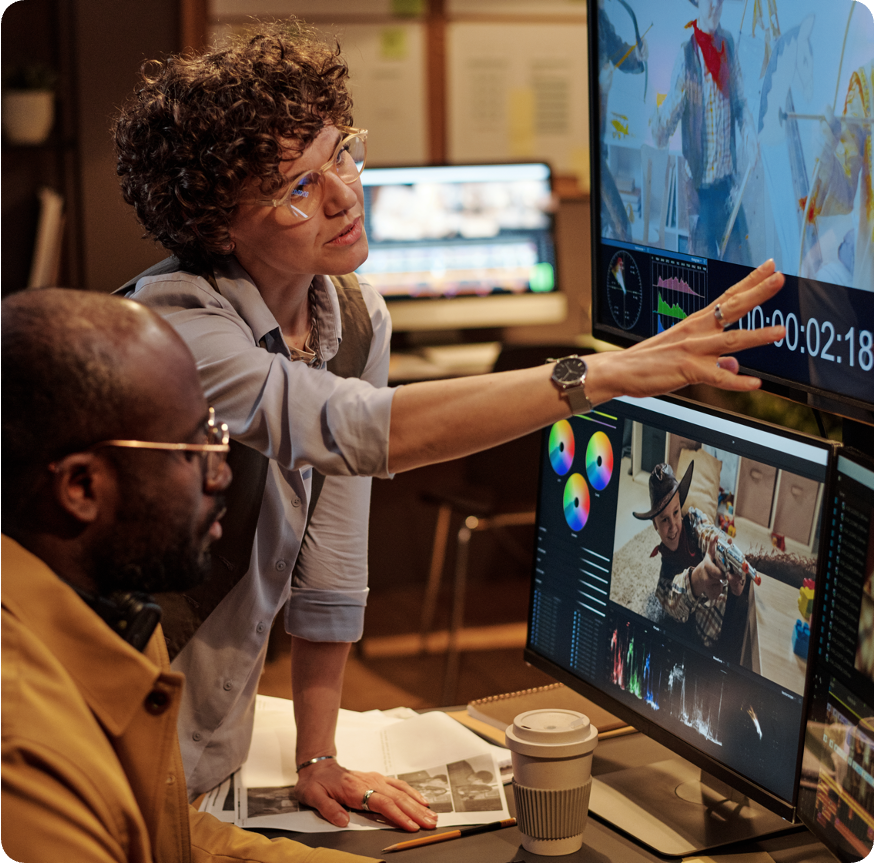 Two people at a cutting station, one pointing at a monitor with a video timeline and colour wheels