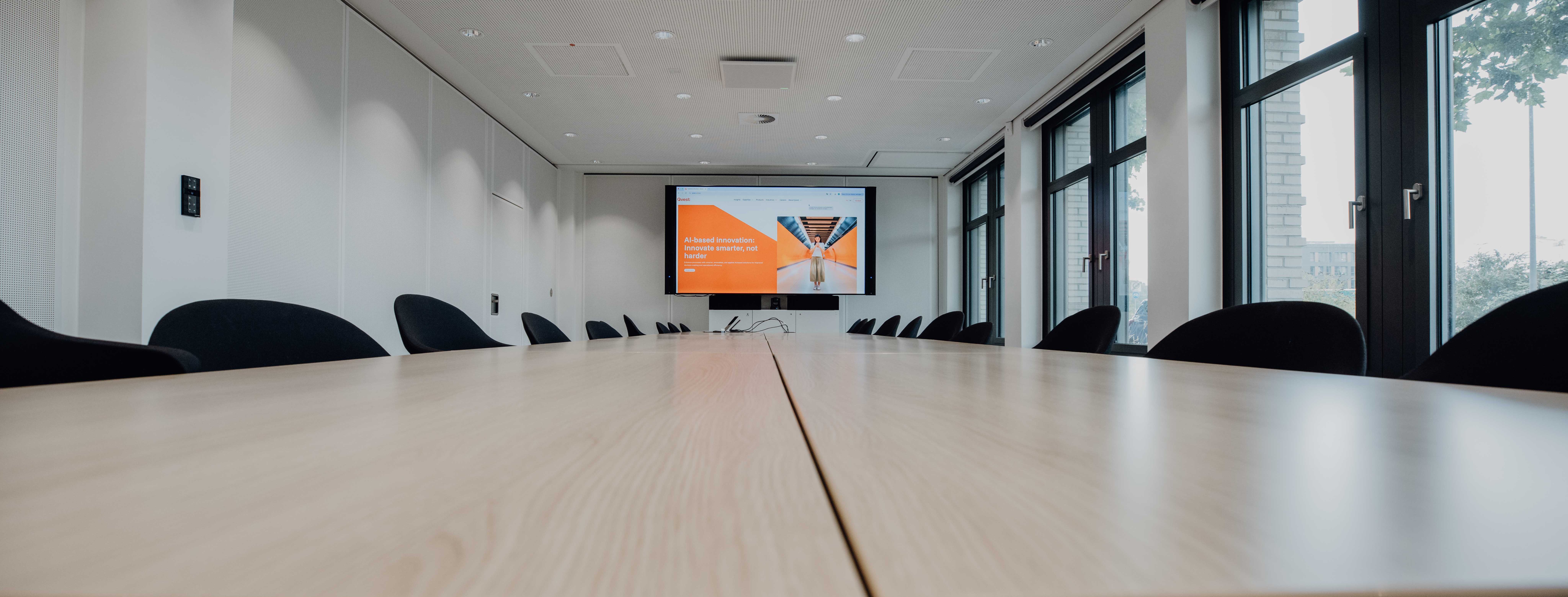 Close Up of modern conference room with a long wooden table, black chairs, and a large screen for presentations.