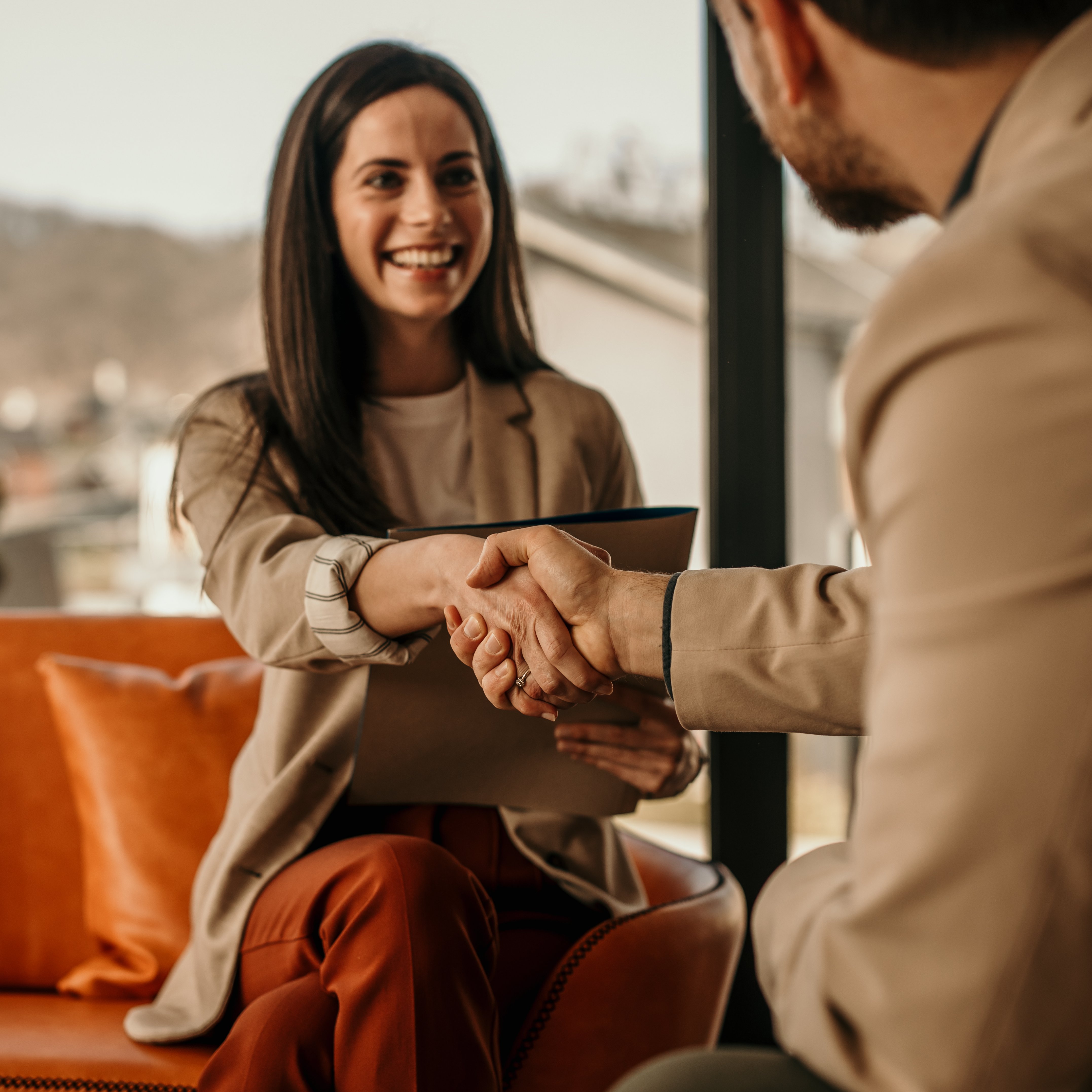 Zwei Geschäftspartner geben sich lächelnd die Hand in einem modernen Büro.