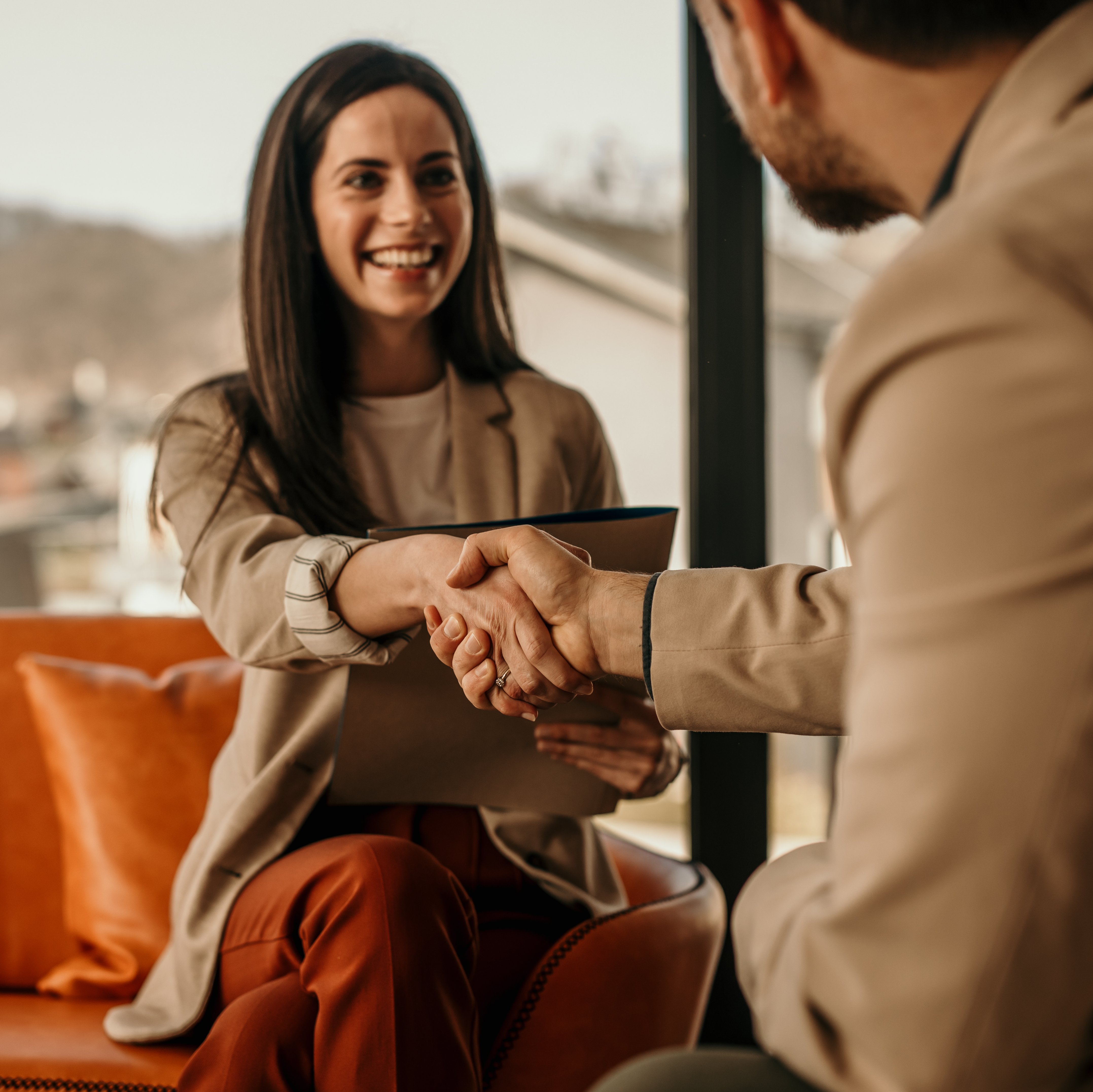 Two business partners smiling and shaking hands in a modern office.