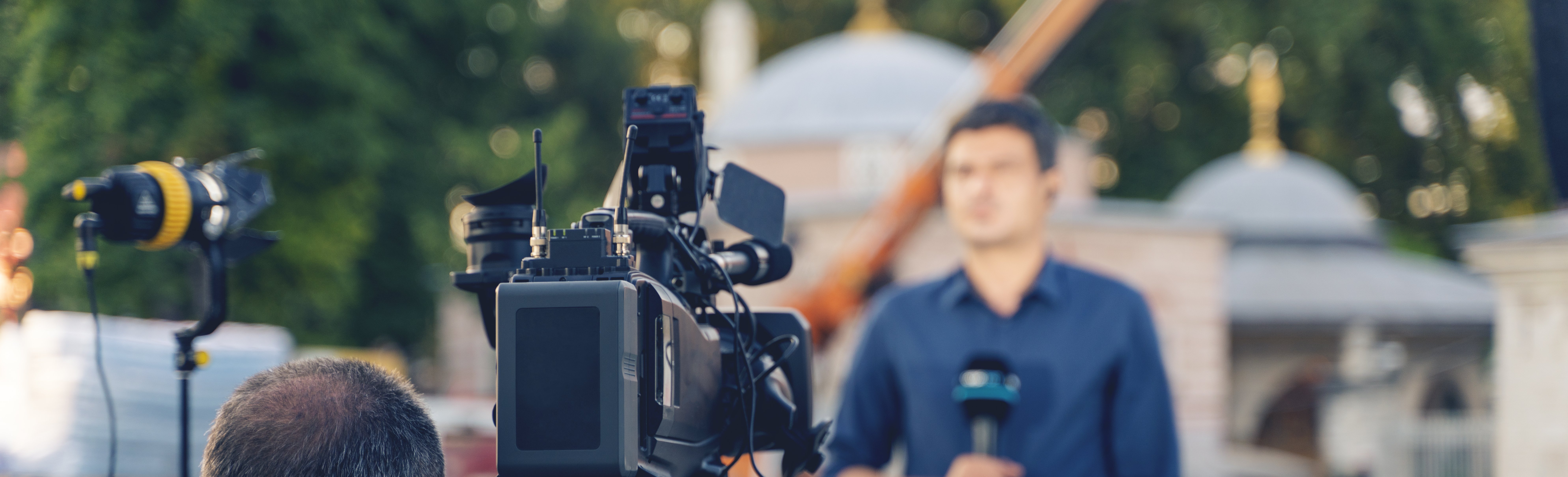 Camera crew filming a reporter during a live broadcast outdoors in front of a historic building.