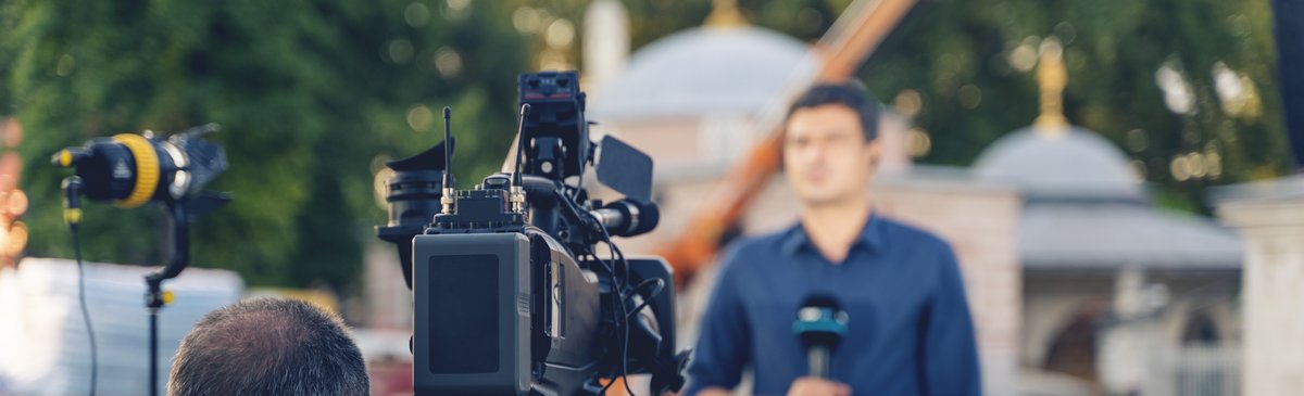 outdoor-live-report.jpg Camera crew filming a reporter during a live broadcast outdoors in front of a historic building.