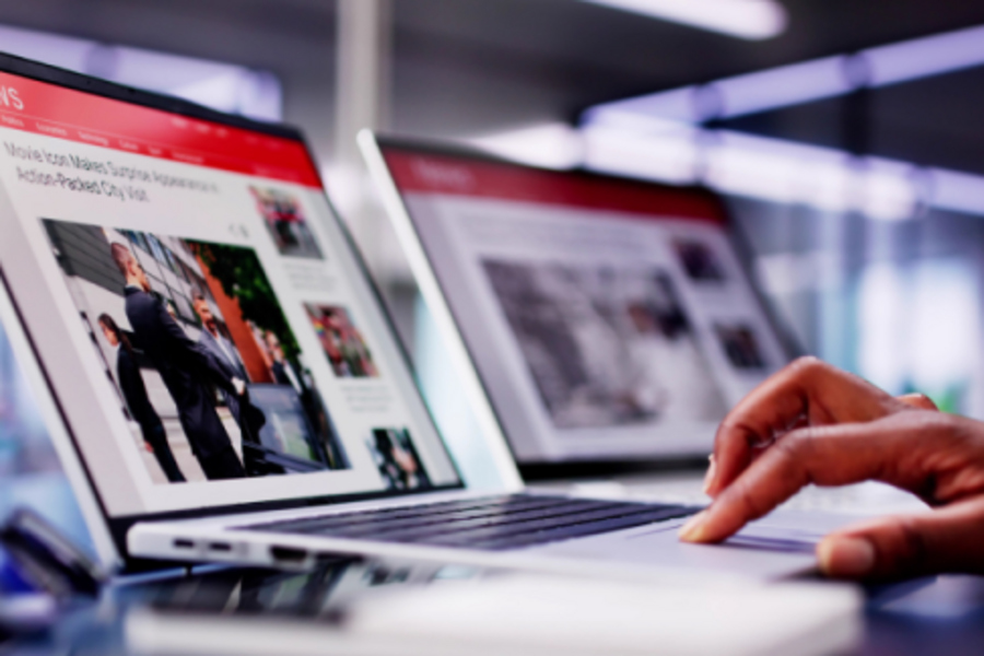 Hand operating a laptop displaying news websites in a modern work environment.