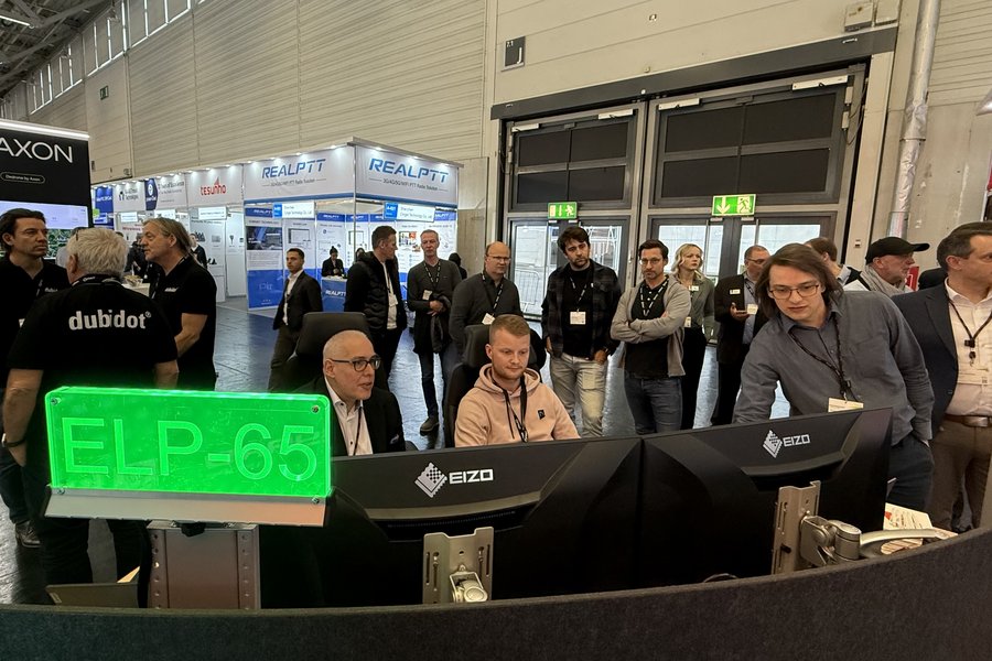 Visitors interacting with monitors and people at the Qvest booth, PMRExpo 2025.