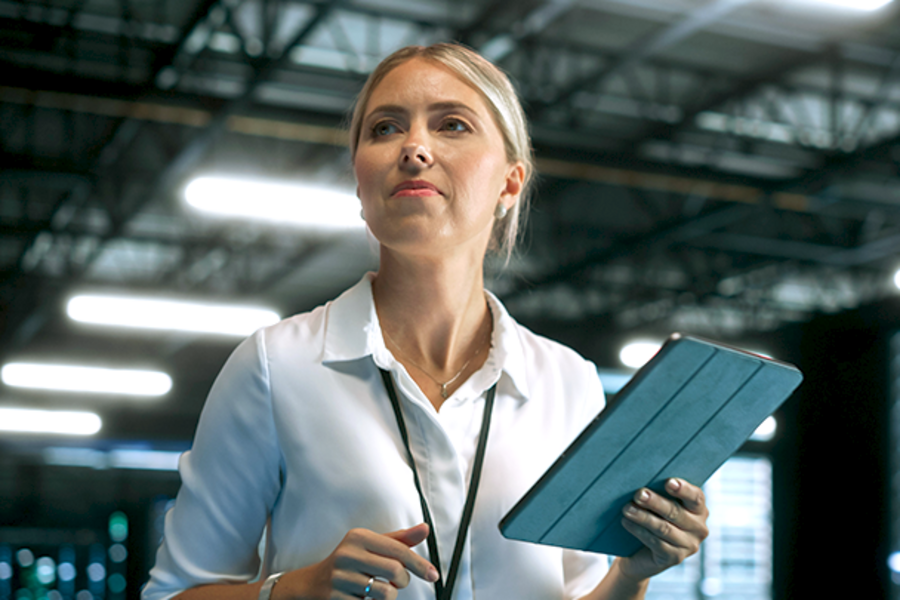 Woman holding a tablet and looking focused in a modern industrial or technology environment.