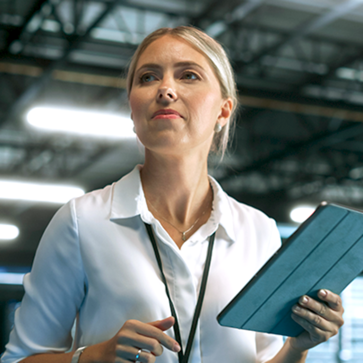 Woman holding a tablet and looking focused in a modern industrial or technology environment.