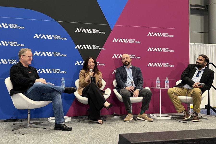 Discussion panel at the NAB Show New York with four people seated on stage in front of colorful event backdrops.