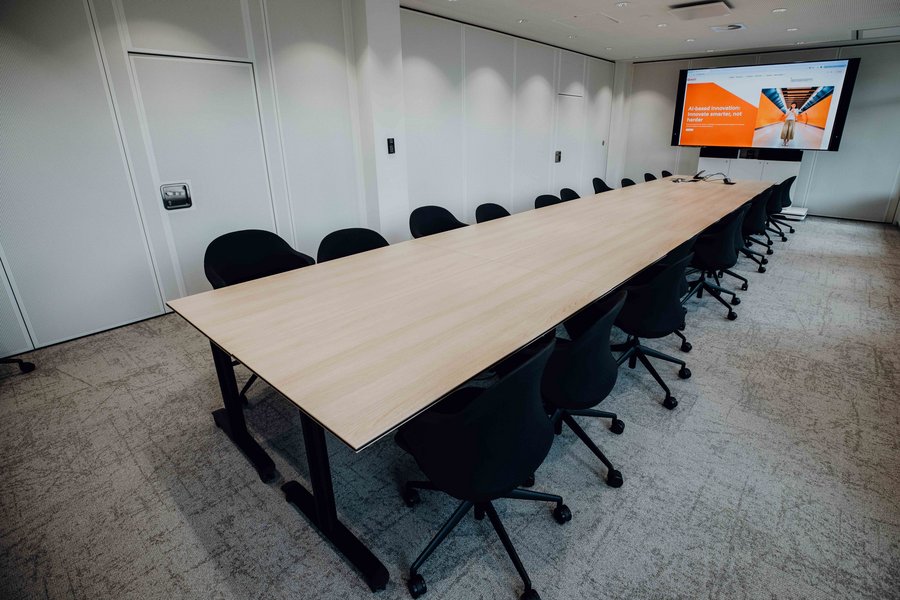Modern conference room with a long wooden table, black chairs, and a large screen for presentations.