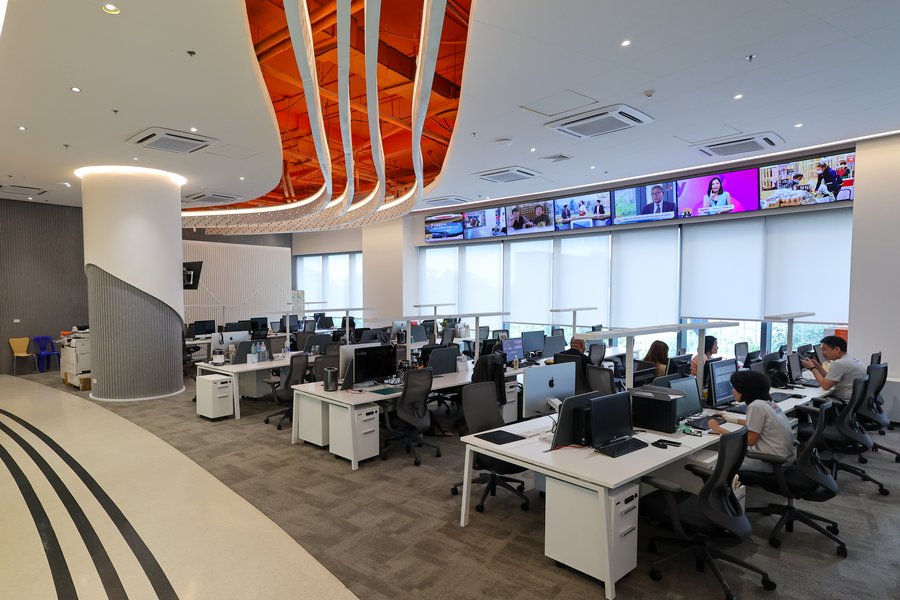 Modern news office with active workstations and media content displays.