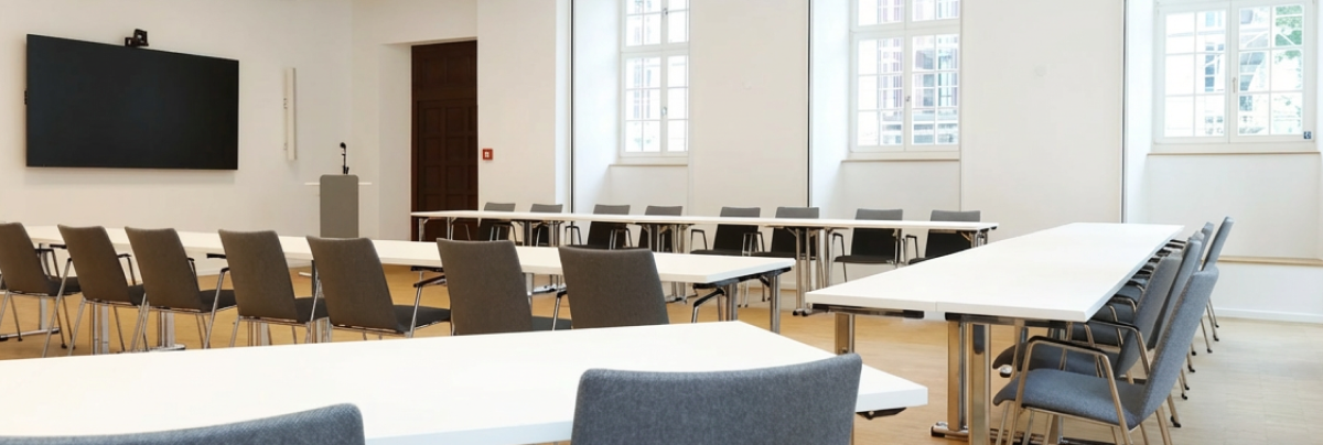 Bright conference room with U-shaped table setup, chairs, and a presentation screen.