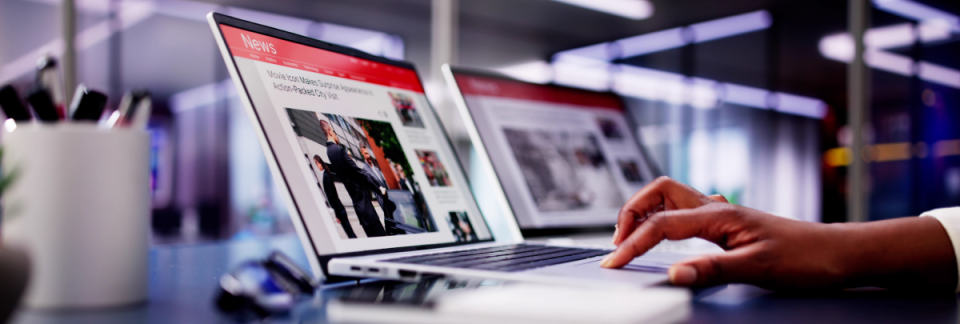 Hand operating a laptop displaying news websites in a modern work environment.