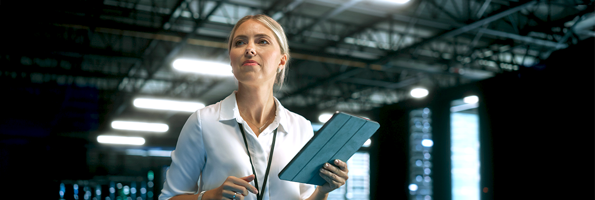 Woman holding a tablet and looking focused in a modern industrial or technology environment.