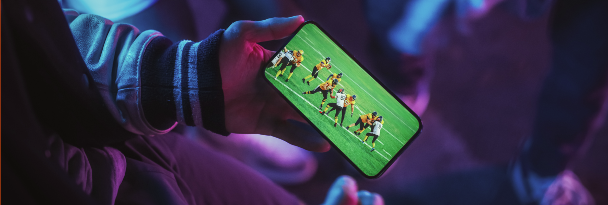 A person holding a smartphone while watching a live sports broadcast of an American football game.