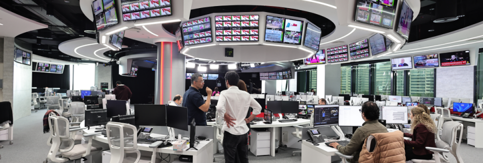 Modern newsroom with multiple monitors and staff working on editorial tasks.